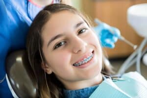 A teenage girl with braces smiling while sitting in the dentist's chair